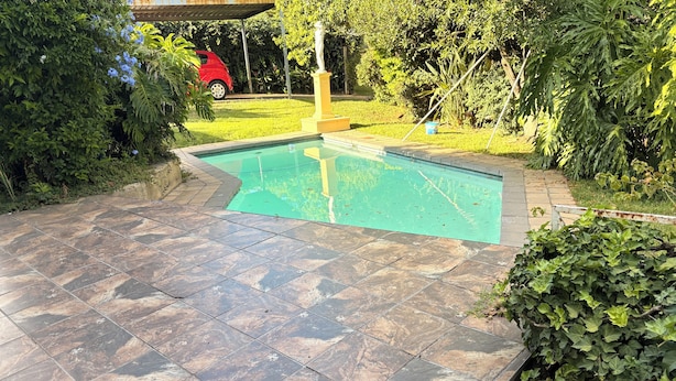 Une piscine dotée d’une terrasse carrelée, entourée de verdure et ornée d’une statue.