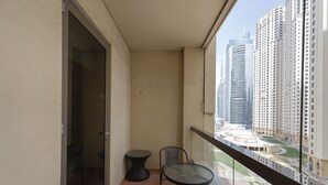 A balcony with a table and chairs, a view of high-rise buildings, and a door leading to an interior space. - Cozy JBR 2BR Retreat Steps to the Beach The Walk (Dubai)