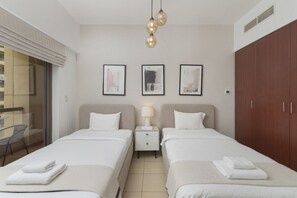 A hotel room with two beds, a nightstand with a lamp, a wardrobe, and framed pictures on the wall. - Cozy JBR 2BR Retreat Steps to the Beach The Walk (Dubai)