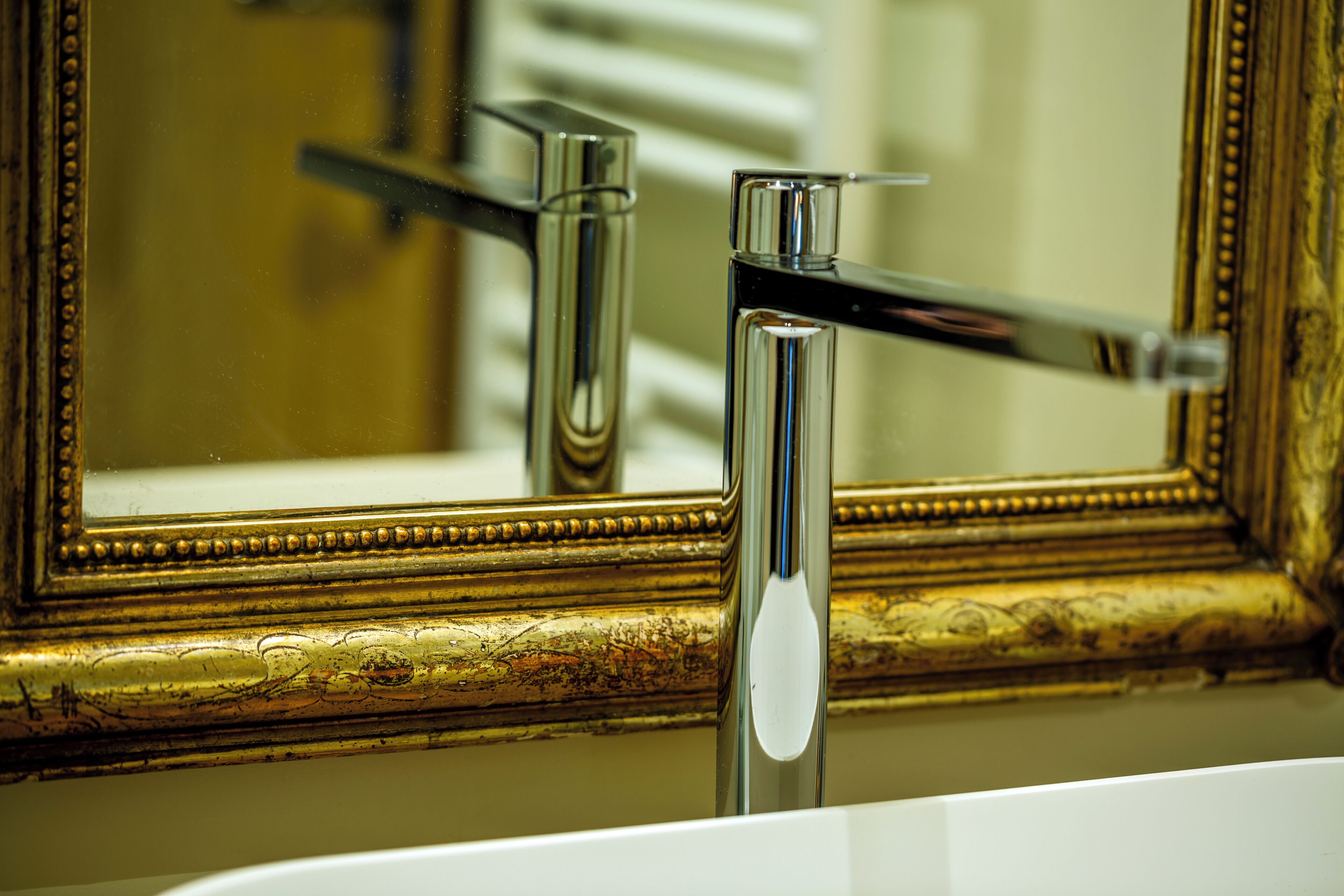 Ein Badezimmer mit einem goldfarbenen Spiegelrahmen, einem Chromarmaturen und einem weißen Waschbecken.