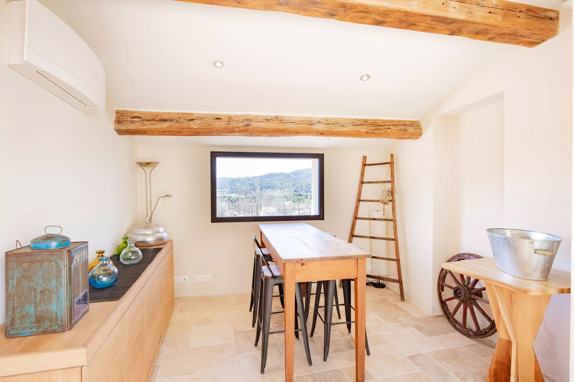 A kitchen with a wooden table, chairs, a window with a view, a ladder, and a rustic cabinet.
