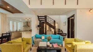 A modern living room with a sofa, coffee table, and a staircase leading to an upper level. - Staymaster Aurum Aqua 3BR Villa  (Vagator)
