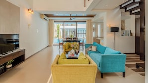 A modern living room with a sofa, a television, and a dining area with a table and chairs. - Staymaster Aurum Aqua 3BR Villa  (Vagator)