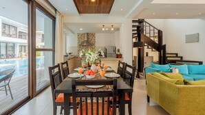 A dining area with a table set for six, a sofa, and a staircase leading to an upper level. - Staymaster Aurum Aqua 3BR Villa  (Vagator)