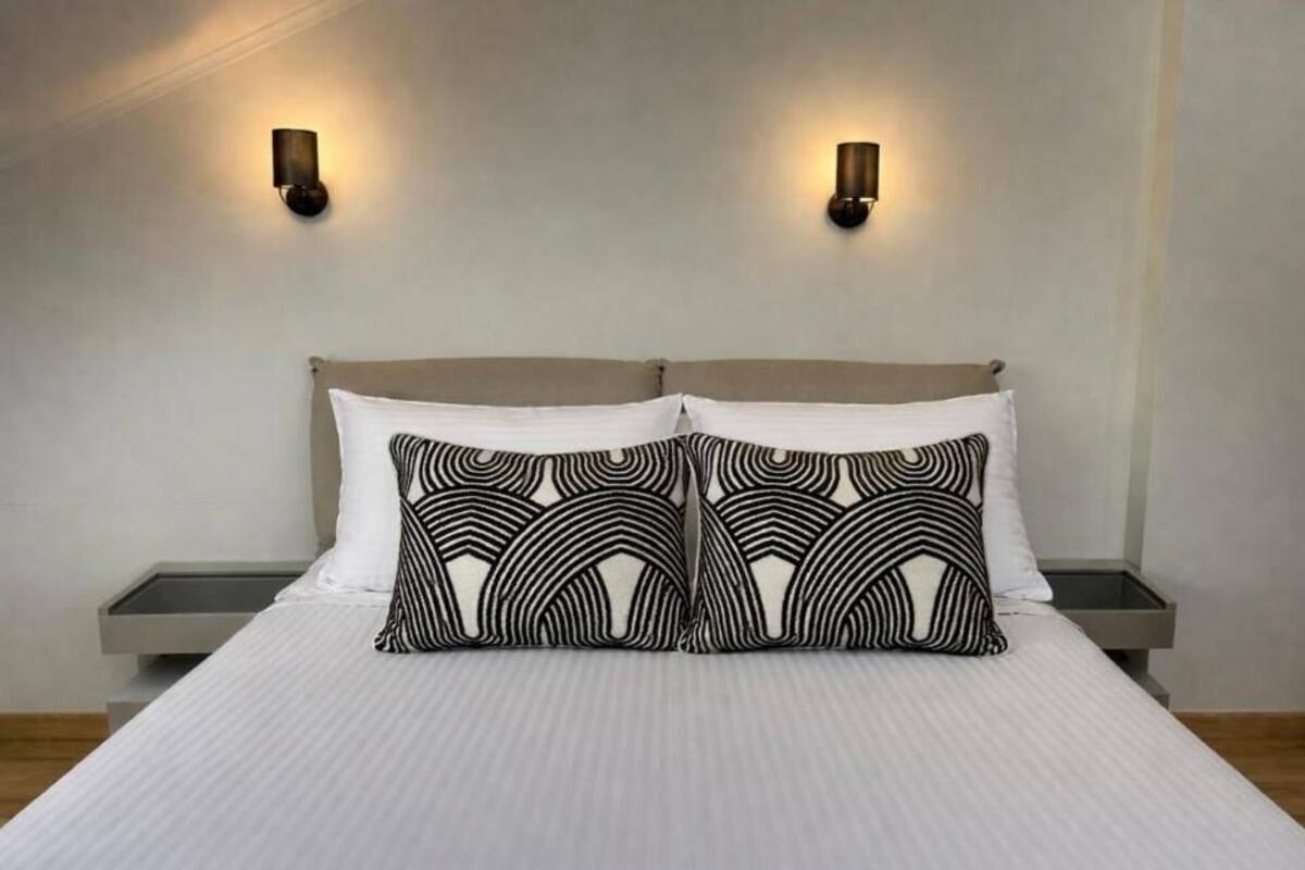 A bed with a striped white bedspread, two black and white patterned pillows, and two wall-mounted light fixtures.