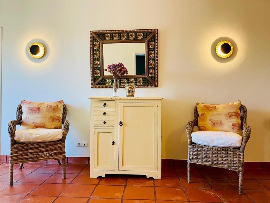 A room with two wicker chairs, a cabinet, and a mirror with wall sconces.
