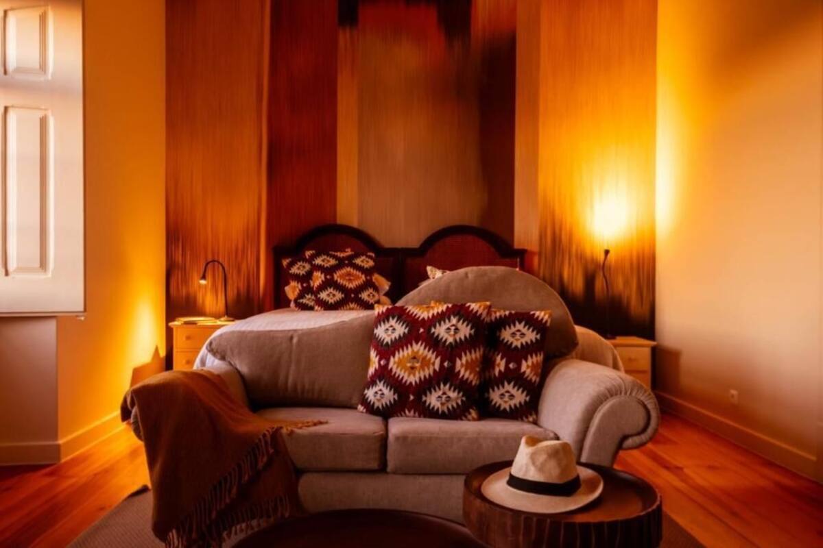 A bedroom with a bed, a sofa, a bedside table, and a hat on a small table.