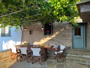 An outdoor dining area with a stone wall, a table with chairs, and a view of the sea.