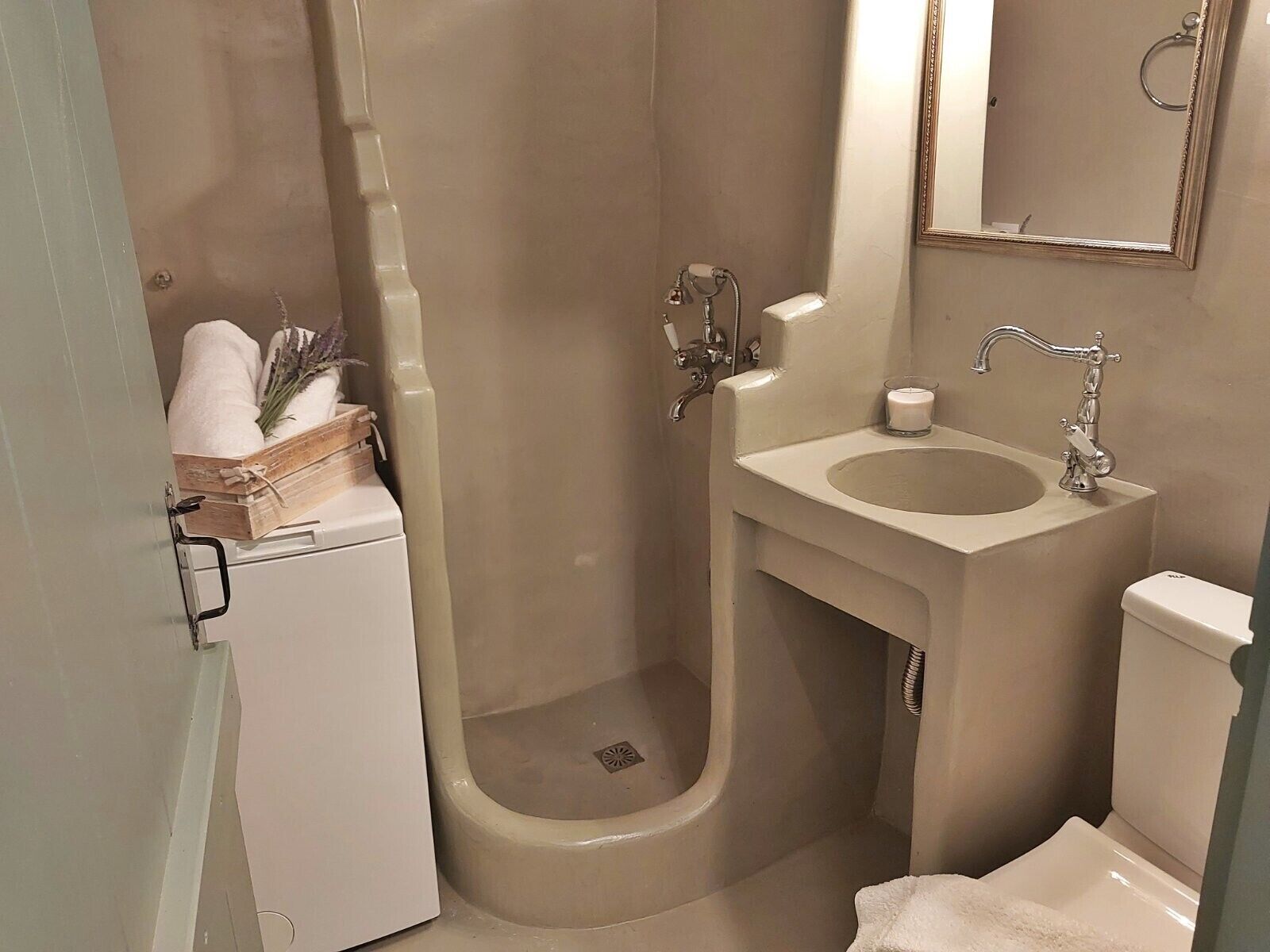 A bathroom with a shower, sink, toilet, and a small wooden box with towels and a plant.