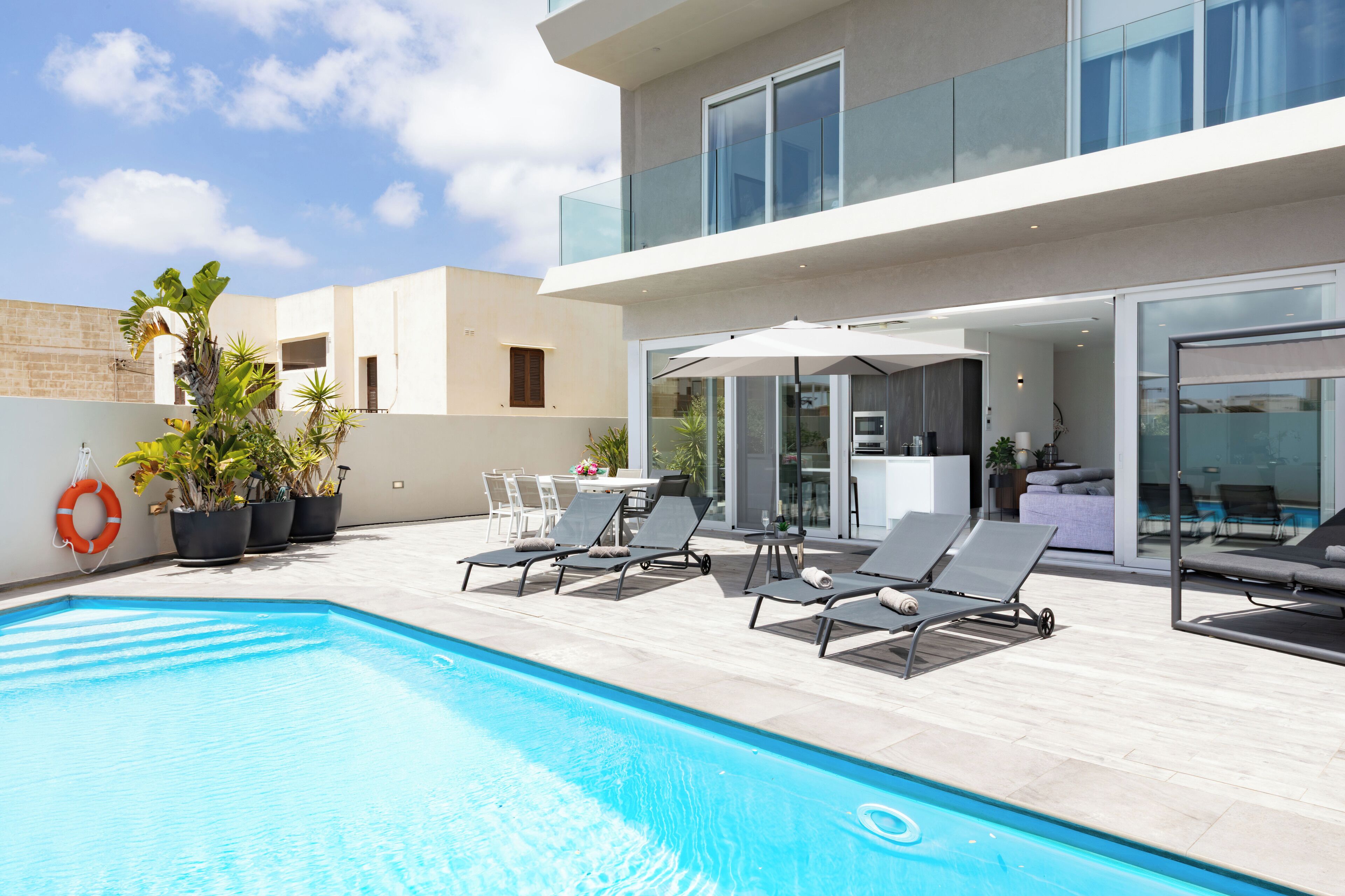 A modern outdoor pool area with lounge chairs, potted plants, and a glass balustrade.