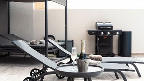 Una terraza en la azotea con sillones de descanso, una mesa con una botella de champán y una copa, y una parrilla.