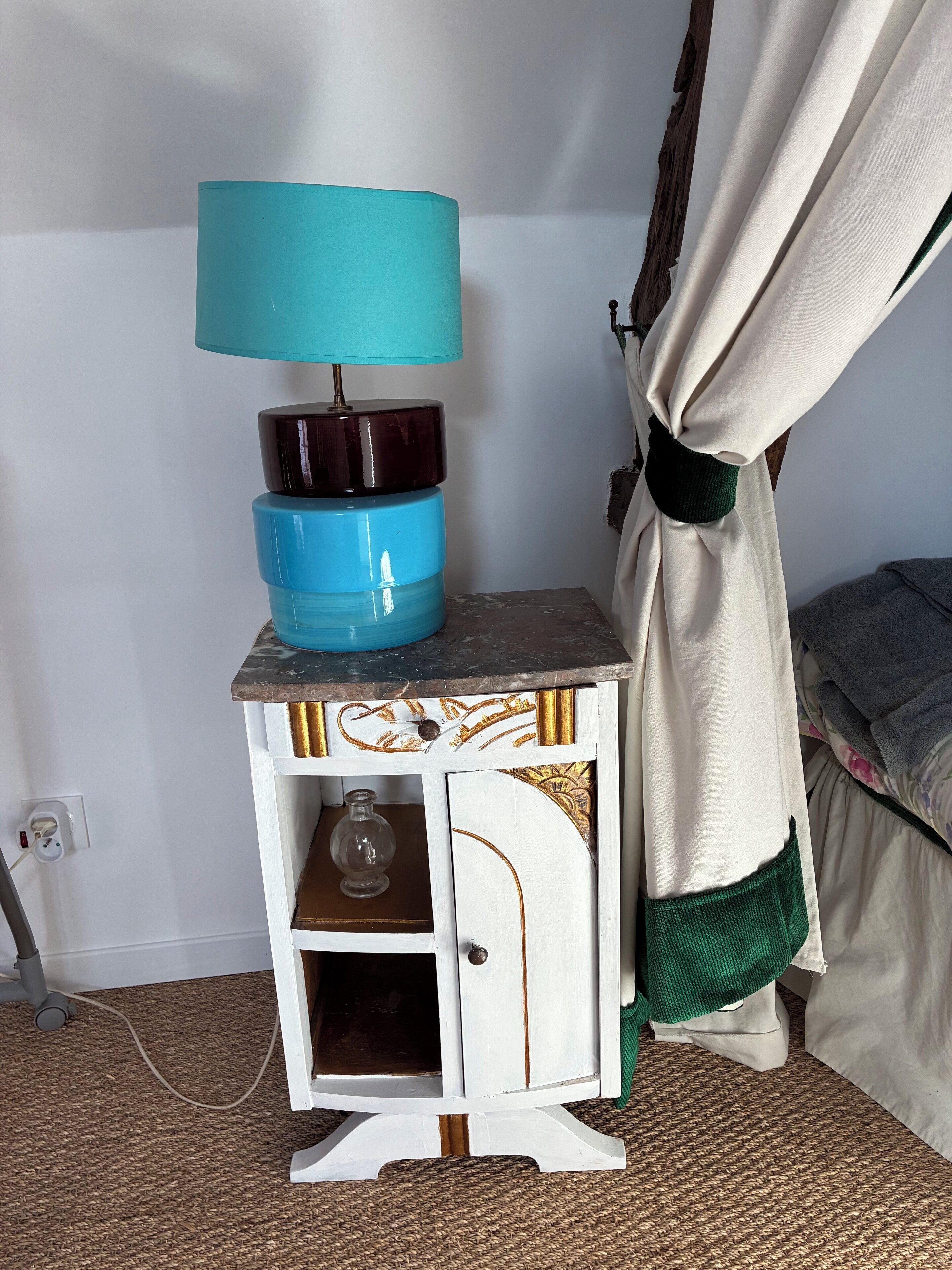 Une petite table de chevet avec une lampe, un récipient en verre et une prise électrique.
