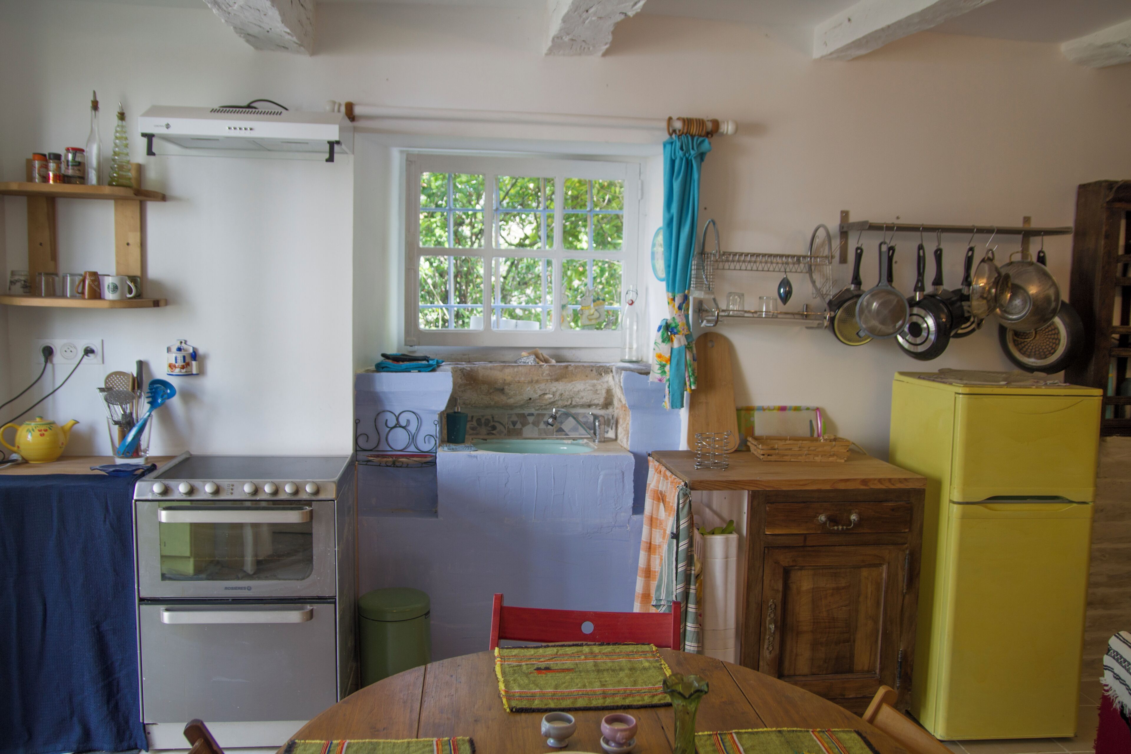Una cocina con ventana, dos hornos, un refrigerador y diversos utensilios.