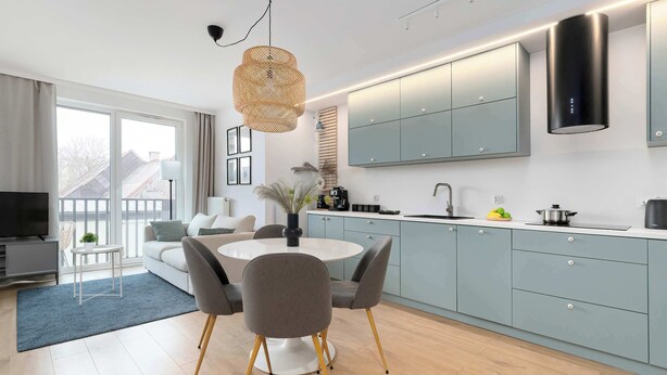 A modern kitchen with grey cabinets, a dining area with a round table and chairs, and a large window. - Secluded Studio in Gdansk | Private Parking and Balcony (Gdańsk)