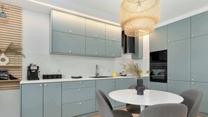 A modern kitchen with grey cabinets, a white countertop, a round dining table, and grey chairs. - Secluded Studio in Gdansk | Private Parking and Balcony (Gdańsk)
