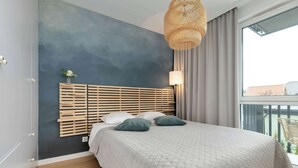 A bedroom with a bed, a headboard, a bedside table, a lamp, a window, and a view of the outside. - Secluded Studio in Gdansk | Private Parking and Balcony (Gdańsk)
