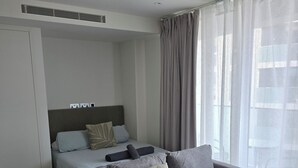 Een moderne slaapkamer met een grijze bank, een bed met grijs beddengoed en een groot raam met dunne gordijnen.
