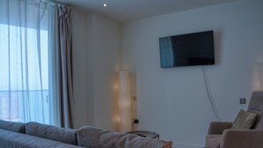 Een moderne woonkamer met een bank, fauteuil, televisie en lamp.