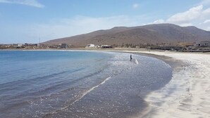 A beach with clear water, a person walking, and a mountain in the background. - Beachfront Bliss in Praia Baixo – 1Min Walk to Sea (Praia Baixo)