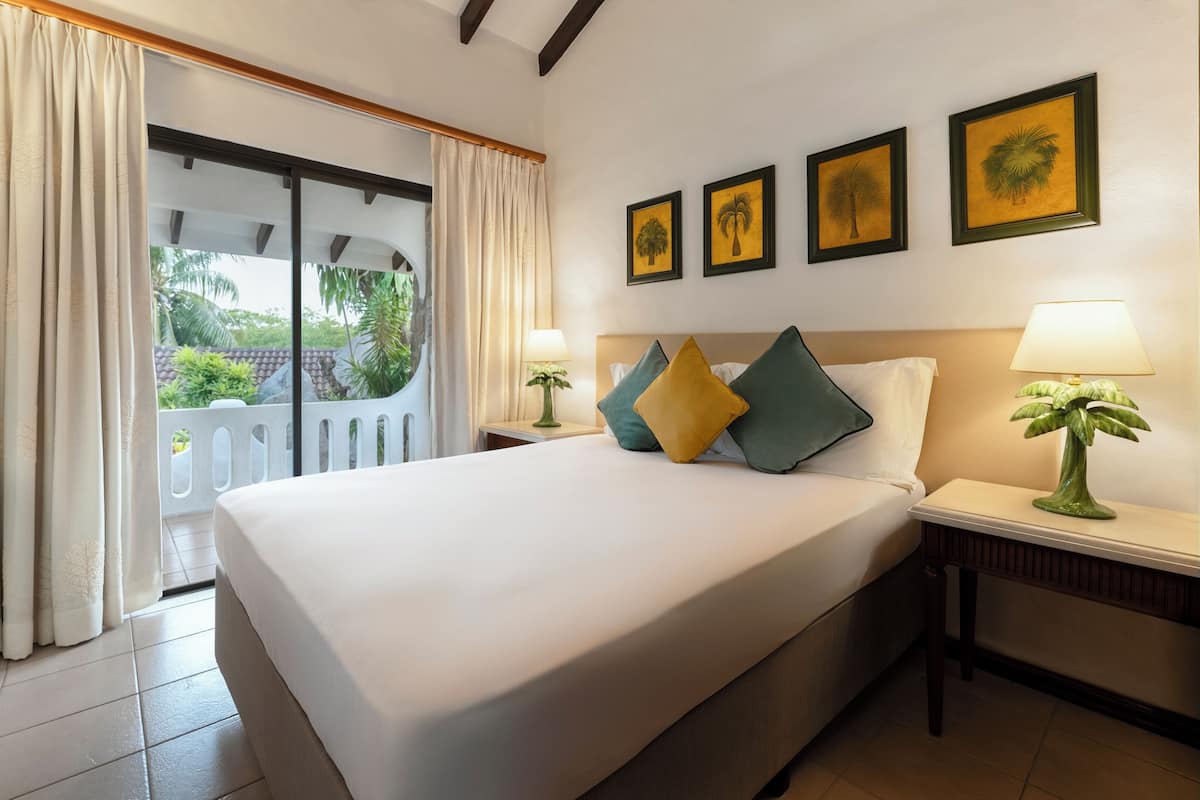Ein Hotelzimmer mit einem großen Bett, zwei Nachttischen, Blick durch eine Schiebetür und drei gerahmten Bildern an der Wand.