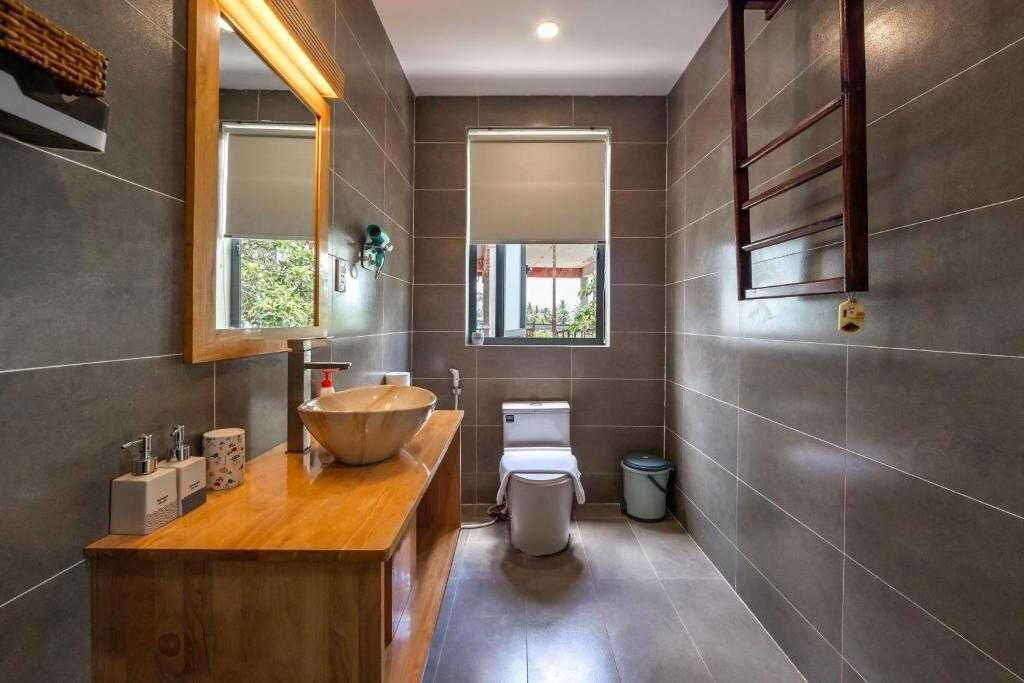 Un baño moderno con tocador de madera, un espejo grande, un lavabo tipo recipiente, un inodoro y una ventana.