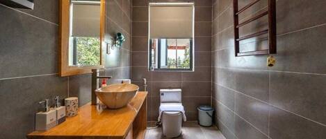 Un baño moderno con tocador de madera, un espejo grande, un lavabo tipo recipiente, un inodoro y una ventana.