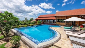 A swimming pool with a tiled edge, surrounded by lounge chairs and a wooden building with a red roof.