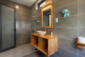 Une salle de bain moderne avec un meuble-lavabo en bois, un grand miroir, un lavabo sur colonne et une douchette à main.
