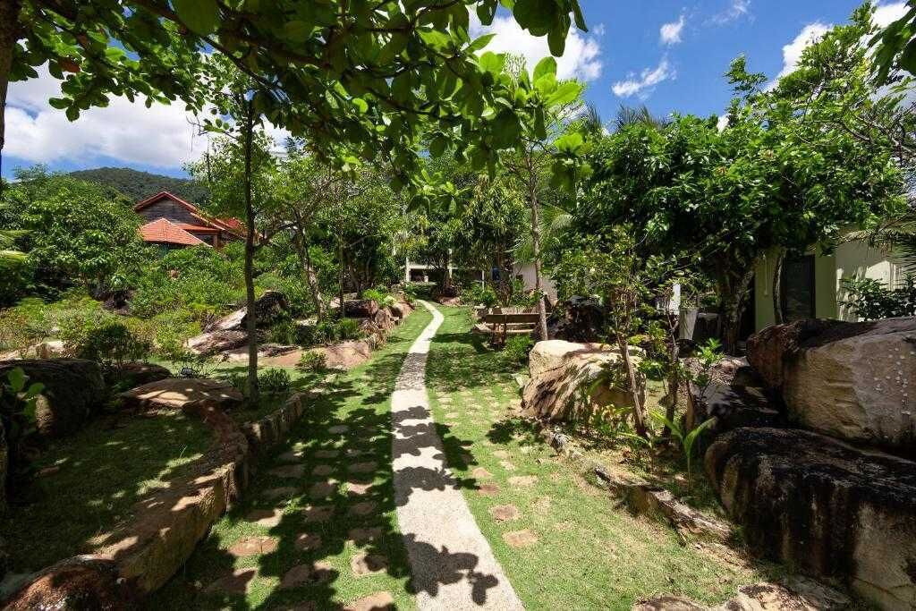 A pathway leading through a lush garden with a house in the background.