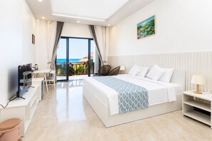 Habitació d'hotel amb llit, escriptori, televisió, vista al mar i un quadre a la paret.