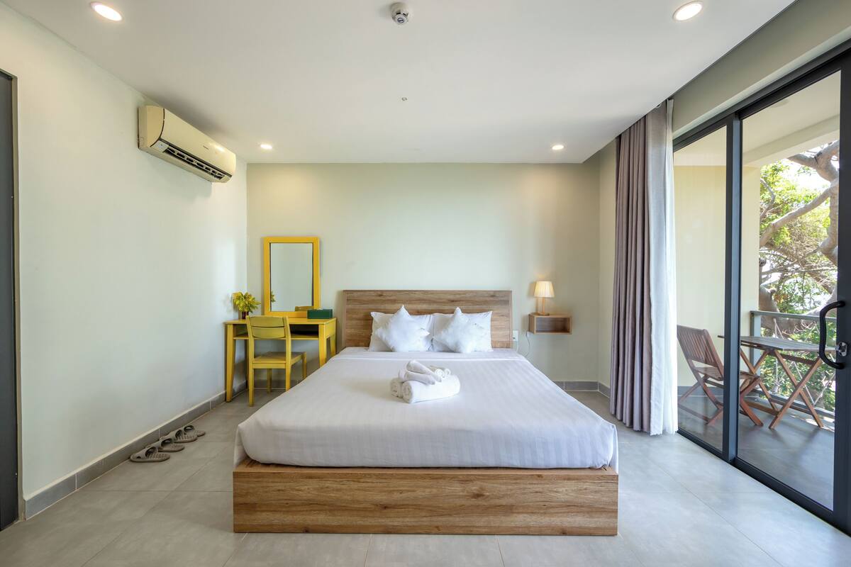 Een moderne hotelkamer met een groot bed, een bureau, een stoel en een balkon met buitenmeubilair.