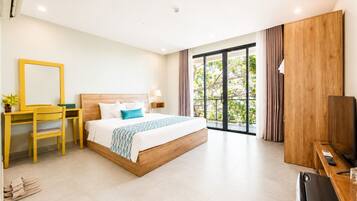 A hotel room with a bed, a desk, a chair, a TV, and a balcony with a view of trees.