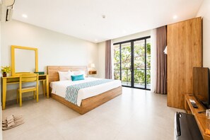 A hotel room with a bed, a desk, a chair, a TV, and a balcony with a view of trees. - Palette Casa De Sol Beach Resort (Phu Quoc)