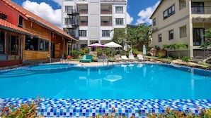 A swimming pool with lounge chairs and umbrellas, surrounded by buildings with balconies and a clear sky.