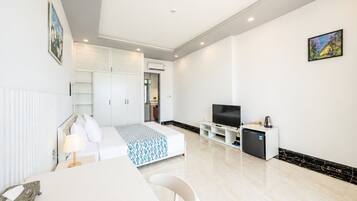 A modern hotel room with a bed, a TV, a mini-fridge, and a dining area.
