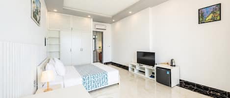 A modern hotel room with a bed, a TV, a mini-fridge, and a dining area.