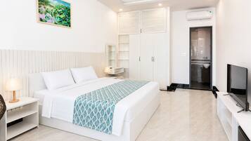 A hotel room with a bed, bedside table, lamp, TV, wardrobe, and a painting on the wall.