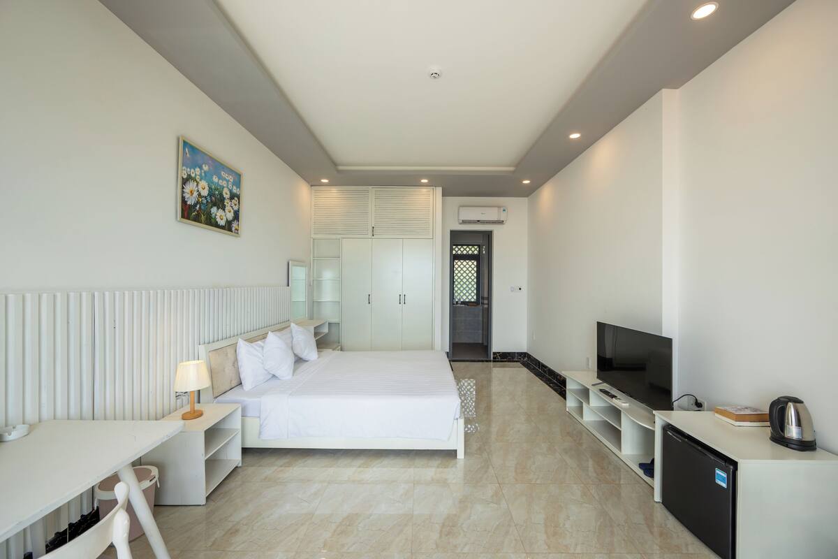 Een moderne hotelkamer met een bed, televisie, bureau en een kleine kitchenette.