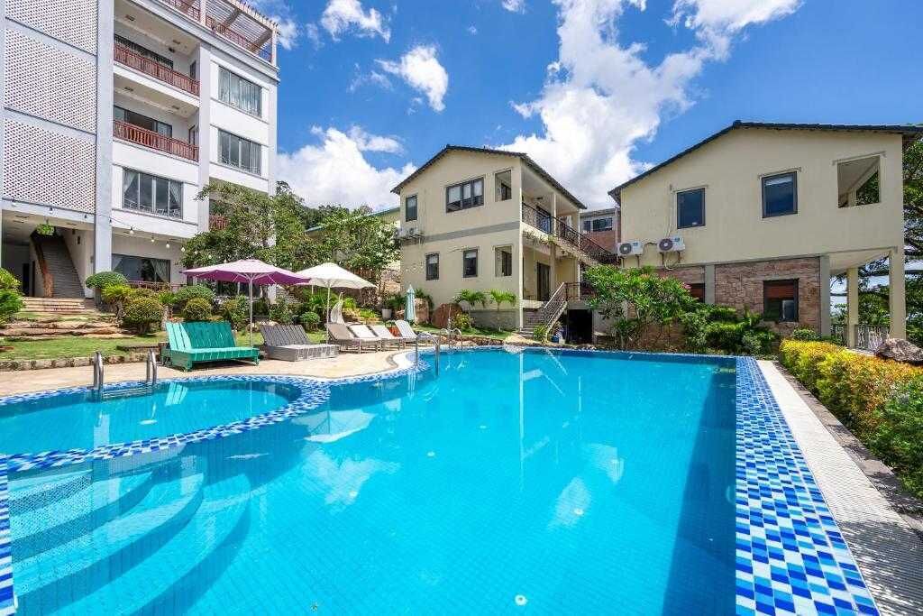 A swimming pool with lounge chairs and umbrellas, surrounded by multi-story buildings with balconies.