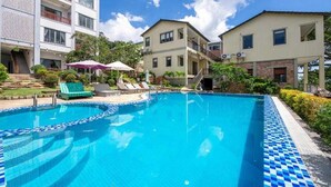 Una piscina con sillones de playa y sombrillas, rodeada de edificios de varios pisos con balcones.