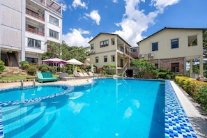 A swimming pool with lounge chairs and umbrellas, surrounded by multi-story buildings with balconies.