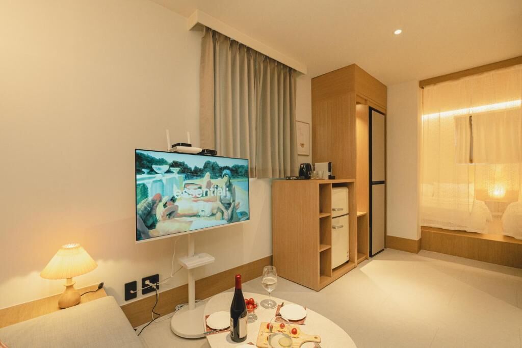 A hotel room with a flat-screen TV, a dining table with wine, and a wooden cabinet.