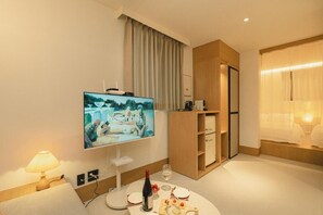 A hotel room with a flat-screen TV, a dining table with wine, and a wooden cabinet. - HOTEL DAUN GURI (Guri)