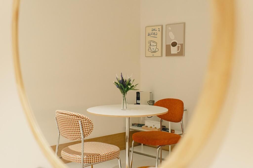 A room with a round table, two chairs, a vase with flowers, and wall art.