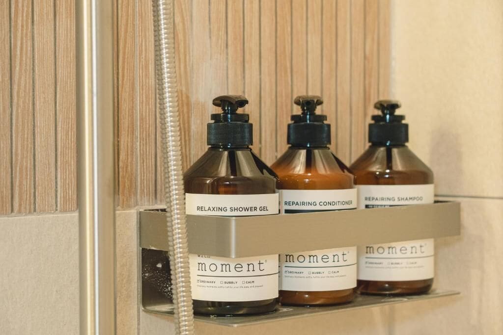 Un estante de baño con tres botellas de gel de ducha, acondicionador y champú de la marca Moment.