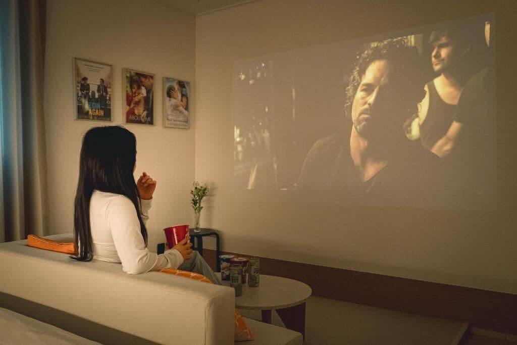 A person sitting on a couch watching a movie on a large screen.