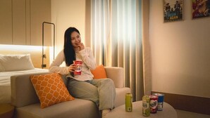 Una habitación de hotel con cama, sofá, una mesita con bebidas y ventana con cortinas.