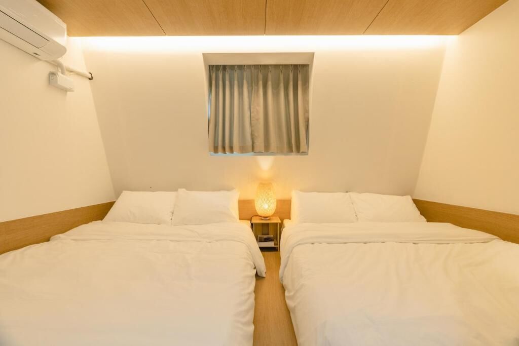 Une chambre avec deux lits, une lampe de chevet, une fenêtre avec des rideaux et un appareil de climatisation.