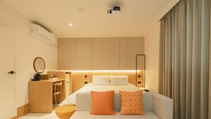 Una habitación de hotel moderna con una cama, mesita de noche, escritorio y un taburete pequeño.