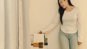 Una persona apoyada en una pared, junto a una mesa con una cesta, una vela y un recipiente.